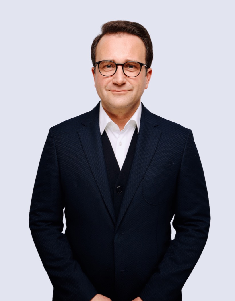 Ein Mann mit Brille, dunklem Anzug und weißem Hemd lächelt in die Kamera.